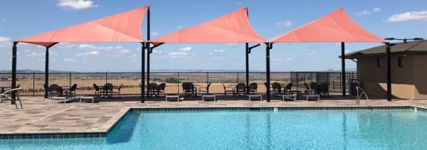 Three salmon colored fabric shades cover the seating area next to a pool.