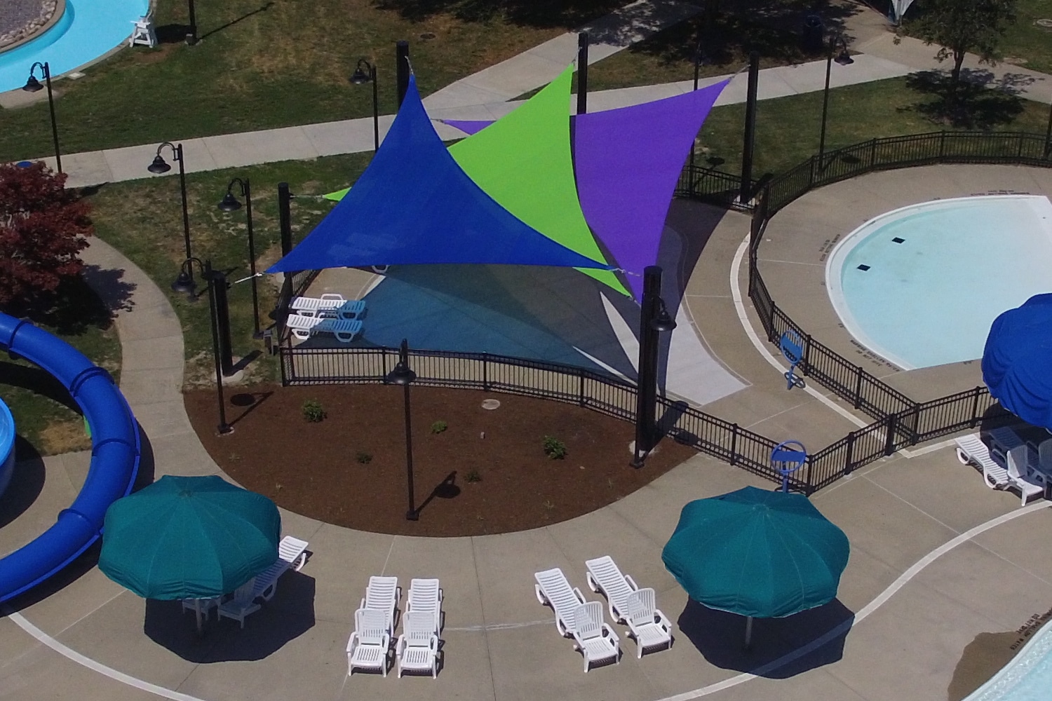 Blue, green and purple triangular sails shade an area at a pool park.
