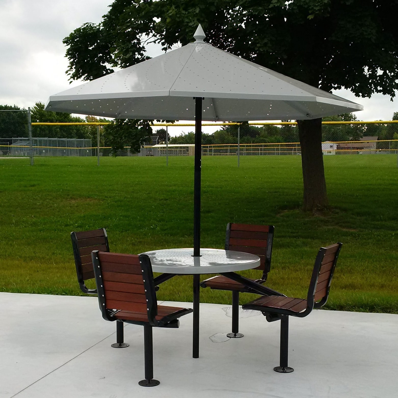 Four wooden chairs connected to an outdoor table with metal umbrella.