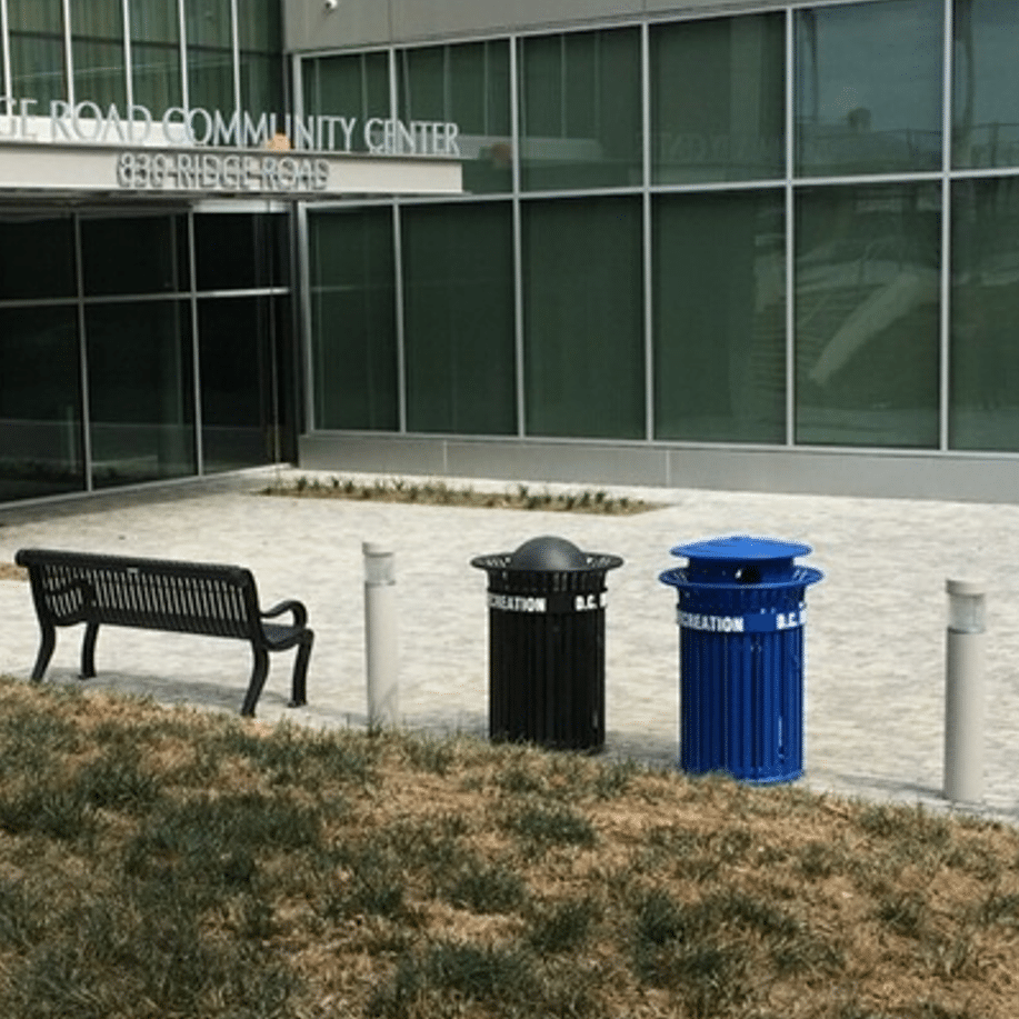 Trash receptacles and a black bench outside a community center