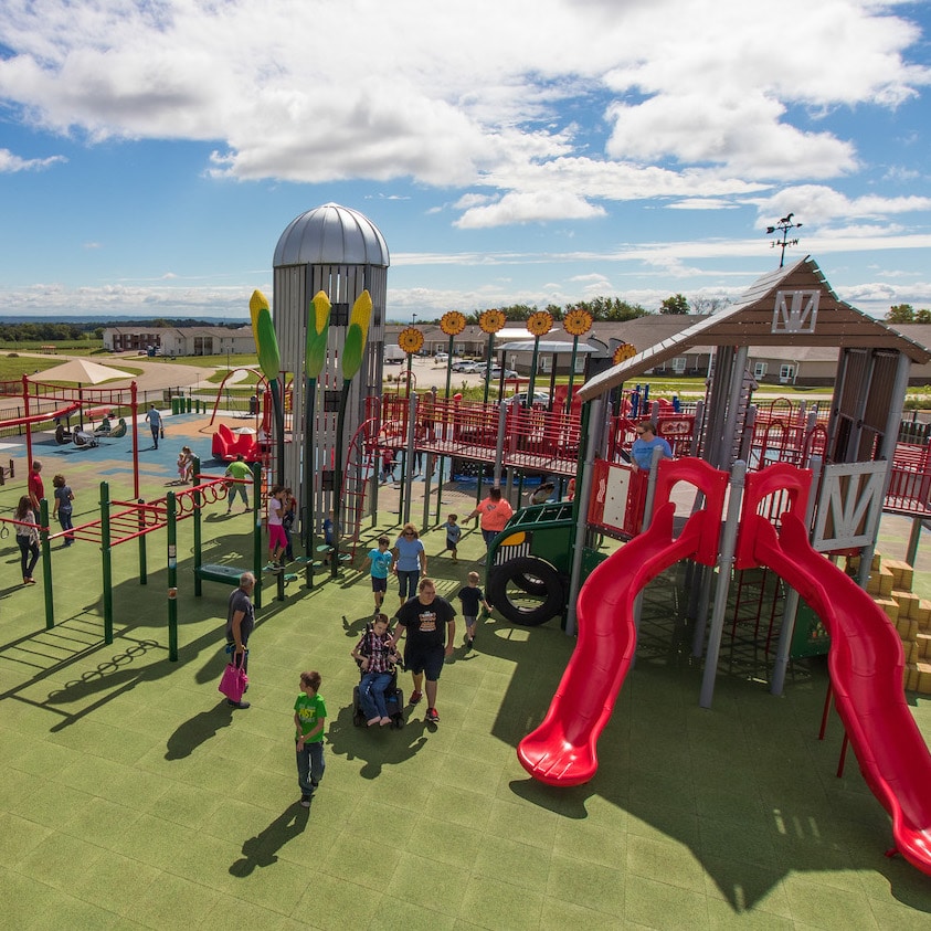 Children and their parents play together on a farm themed inclusive playground.