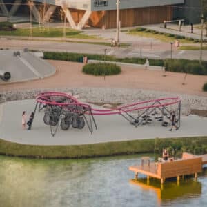 A high-angle view of a modern park showing a long, winding, pink and black net climbing structure.