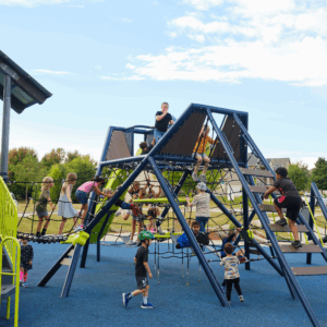 Several children climb and balance on a large, modern net climber with blue and lime green supports on a blue rubber safety surface.