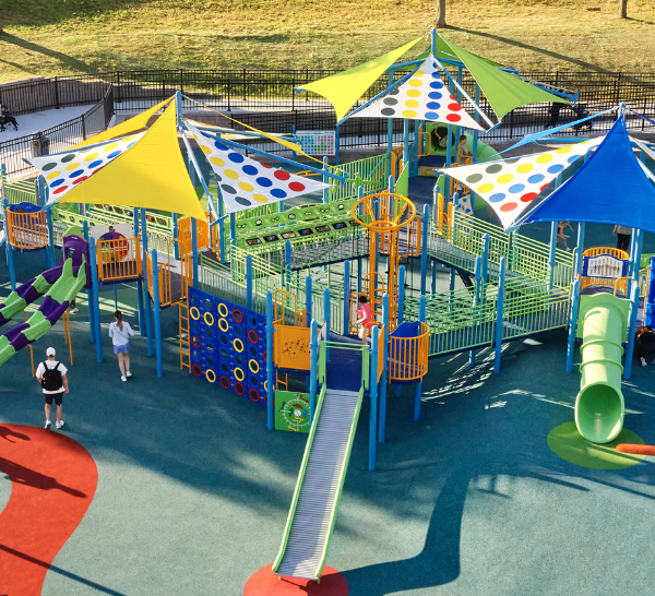 Aerial view of a colorful inclusive playground featuring shade sails, slides, ramps, and accessible surfacing designed for children of all abilities.